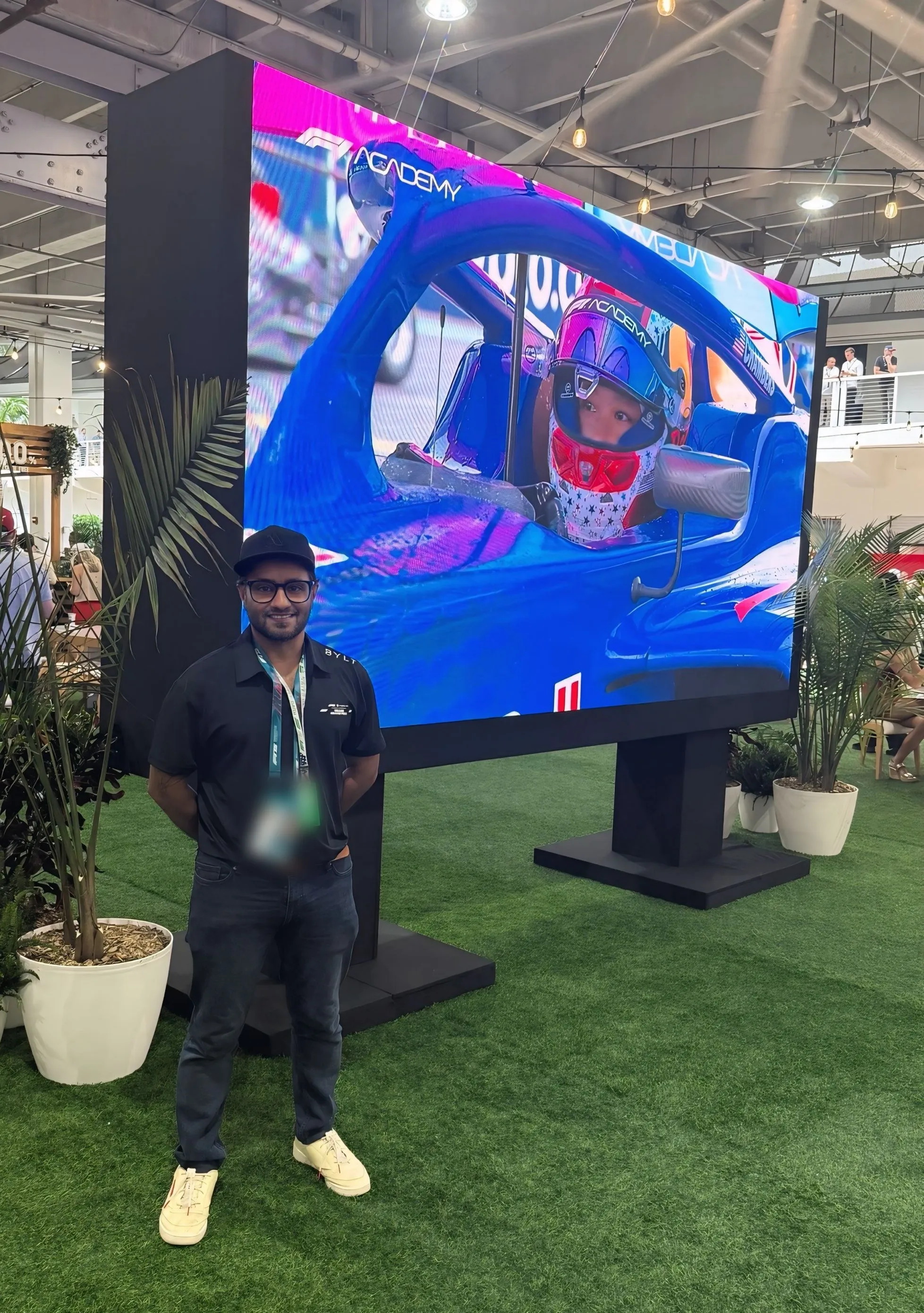 Mahesh Patel beside an LED wall at the Formula 1 Miami Grand Prix, with race coverage on the screen