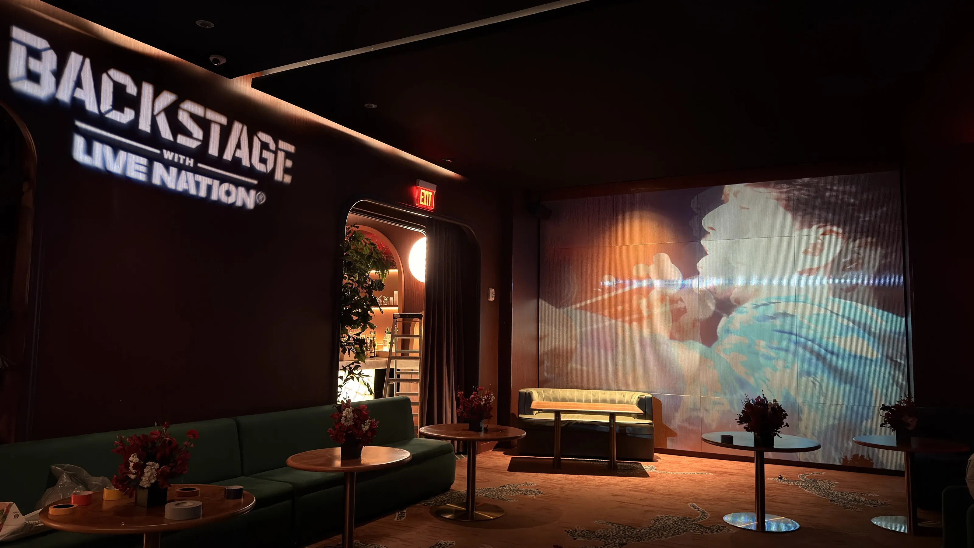 The lounge at The Studio at Maple & Ash, with a tour highlights reel projected across its fluted back wall and the Backstage with Live Nation logo on the wall to the left.