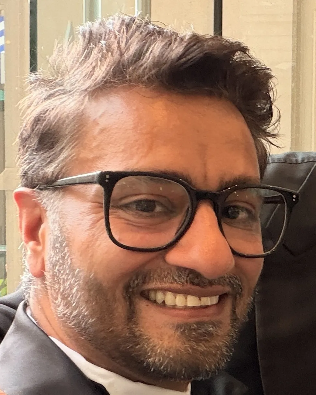 Mahesh Patel, smiling, in glasses and a black tuxedo